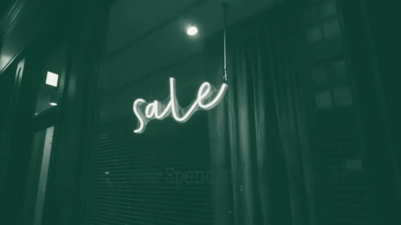 A neon sale sign in a dark shop window
